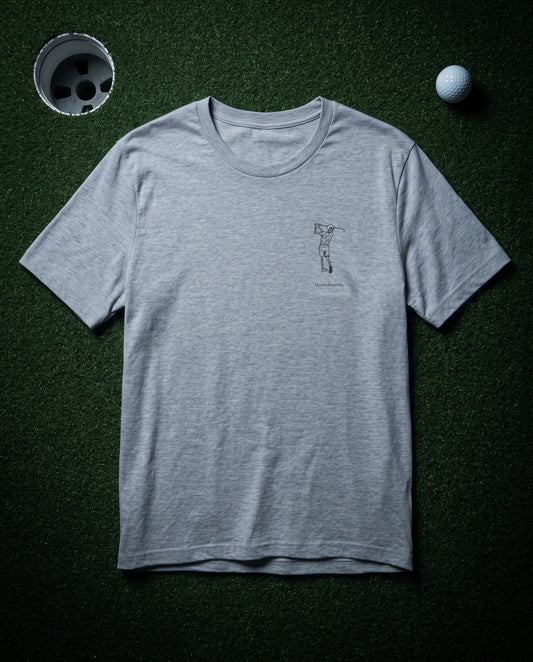 The Bones Tee in Ash — front, Bones chest mark, laid flat on a dark putting green at night