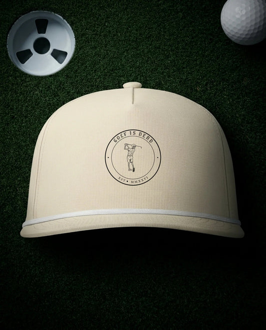 The Emblem Rope Cap in Ivory, laid flat on a dark putting green at night